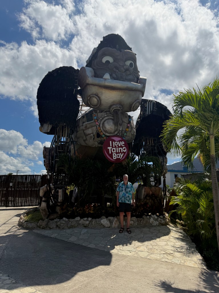 A large decorative statue resembling a Taino figure with a sign reading 'I love Taino Bay' in front of it, with a person standing nearby.