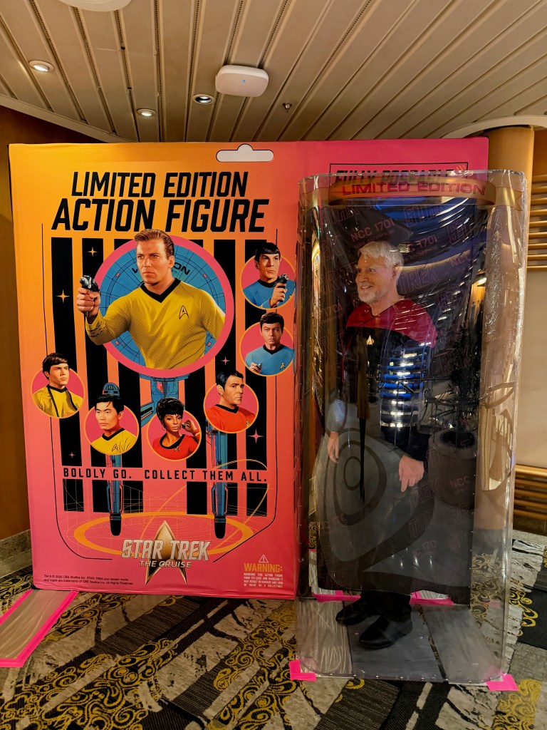 A limited edition Star Trek action figure displayed next to a colorful packaging featuring iconic characters from the franchise. The figure, inside protective packaging, showcases a character in a Starfleet uniform, while the background highlights the phrase 'Boldly Go. Collect Them All.'