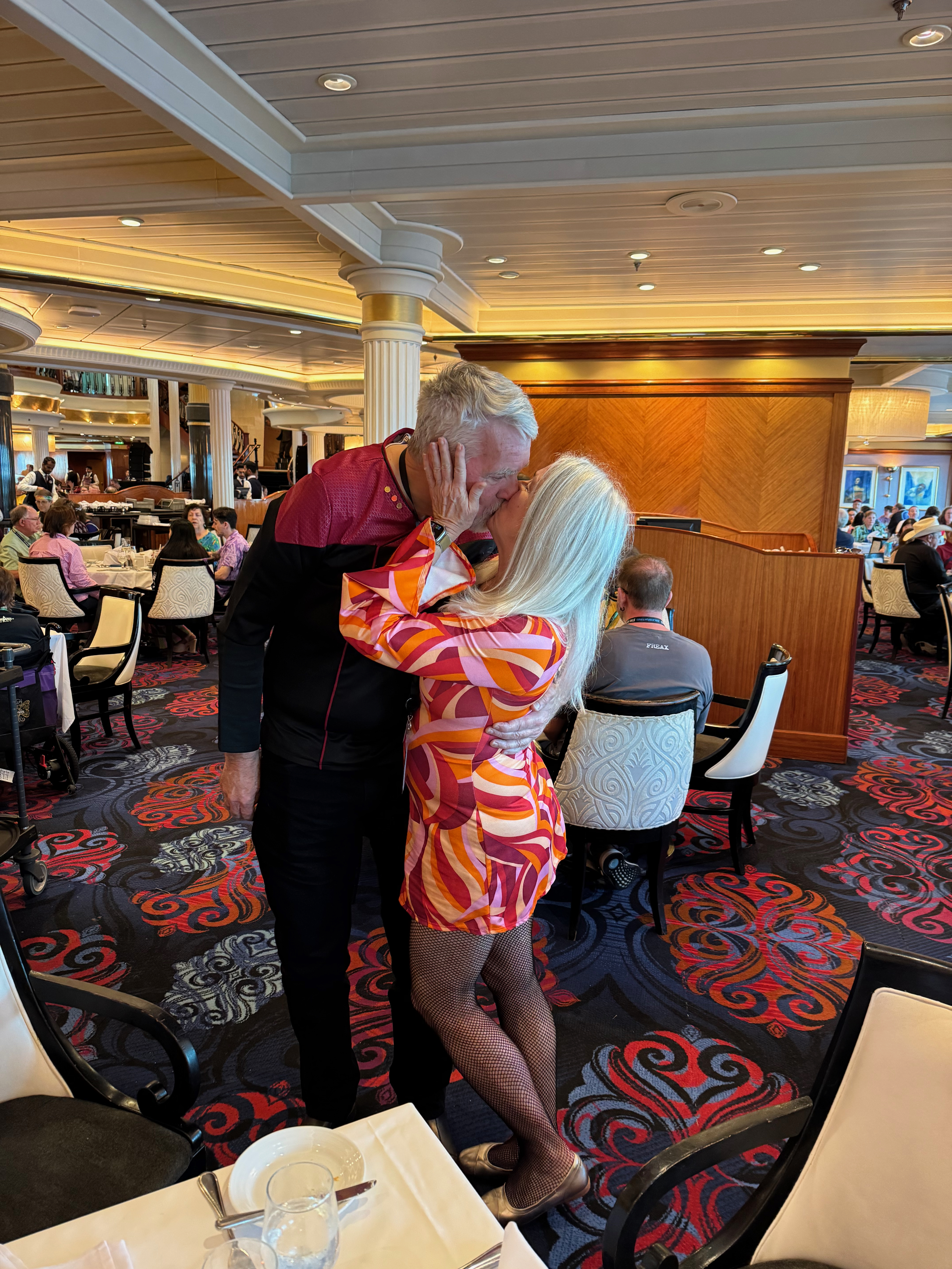 A couple embracing and sharing a kiss in a lively restaurant setting, featuring colorful decor and other diners in the background.